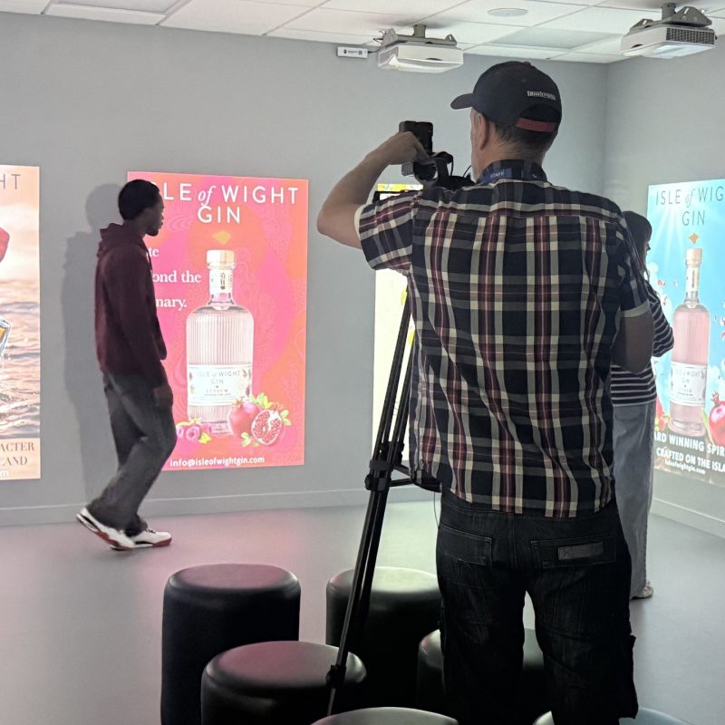 A lecturer takes a photo of a student in front of the artwork projected onto a wall.