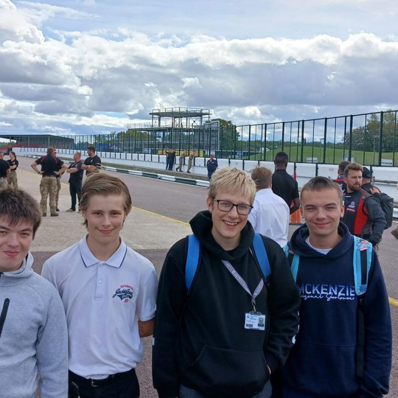 4 Students pose on a roadway with army trucks behind
