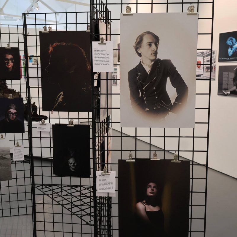 Photography work of people are displayed on a metal rack.