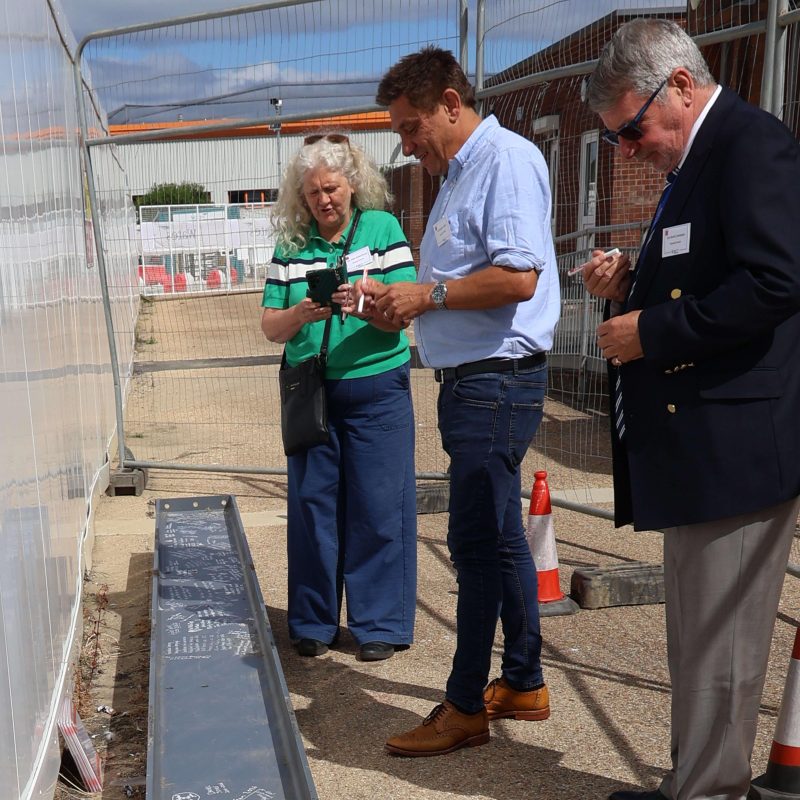 Three councillors stand over a steel beam ready to sign it