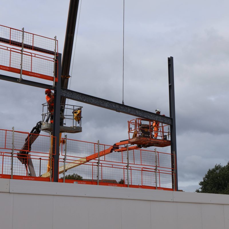 the Steel beam being fitted onto the structure by workers