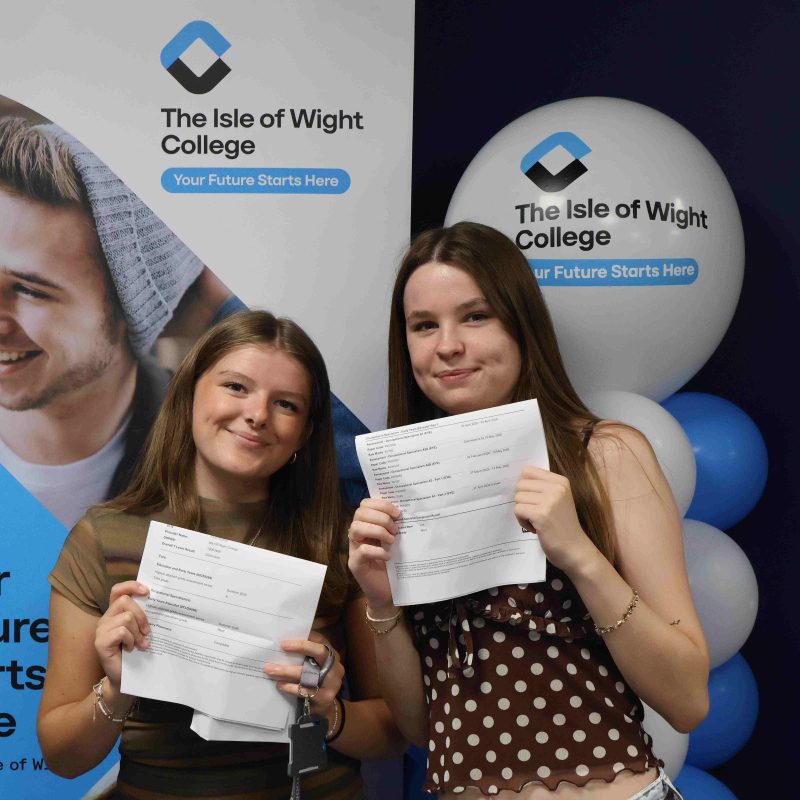 two female students pose in front of balloons with their results