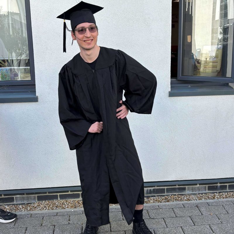 A Student wearing a graduation gown poses for the camera.