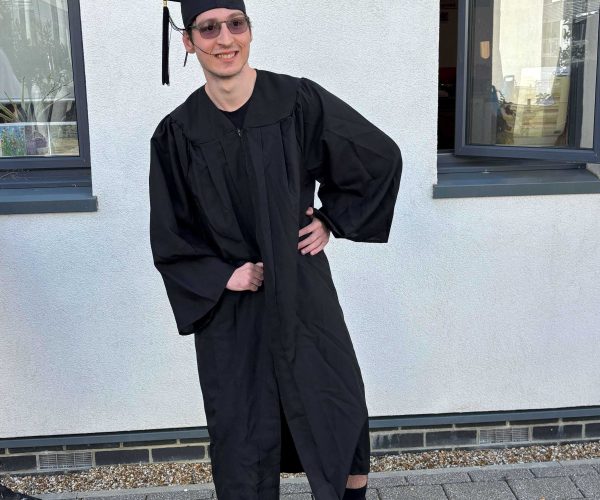 A Student wearing a graduation gown poses for the camera.