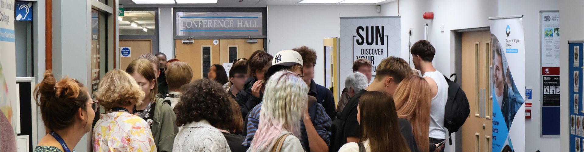 a large crowd of students gather looking at various industry stalls set up in a hallway.