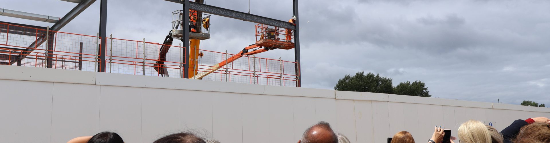 A crowd of people watch as the steel beam is lifted into place