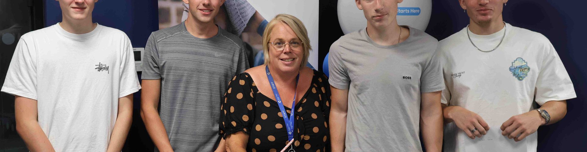 Group of male students stand beside their female lecturer with their results